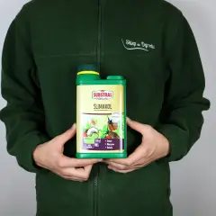 Osoba w zielonej bluzie trzyma butelkę preparatu Ślimakol, który chroni owoce, warzywa i kwiaty przed ślimakami.