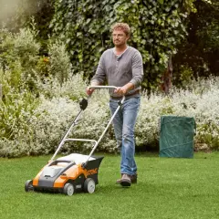 Mężczyzna z wertykulatorem Stihl dba o trawnik. W tle bujna zieleń i kwitnące krzewy.