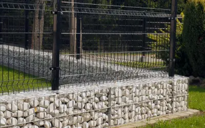 Nowoczesne ogrodzenie z czarną siatką na kamiennych gabionach. To świetne rozwiązanie co zamiast podmurówki pod ogrodzenie, dodaje elegancji i stabilności.