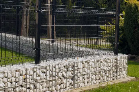 Nowoczesne ogrodzenie z czarną siatką na kamiennych gabionach. To świetne rozwiązanie co zamiast podmurówki pod ogrodzenie, dodaje elegancji i stabilności.