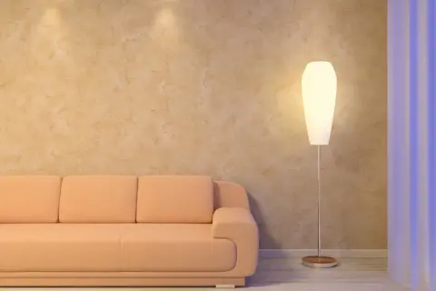 Miękka, brzoskwiniowa kanapa i elegancka lampa stojąca przy ścianie z fakturą przypominającą paca wenecka.