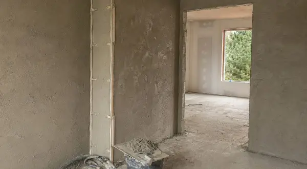 Ściany w trakcie prac wykończeniowych, na których widać świeże tynki cementowo wapienne. W wiadrze przygotowana zaprawa.
