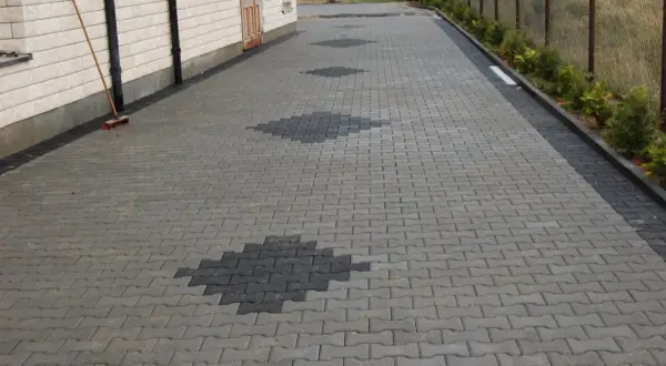 Podjazd z behatonu z ozdobnymi rombami z ciemniejszej kostki. Obok domu miotła czeka na dalsze prace.