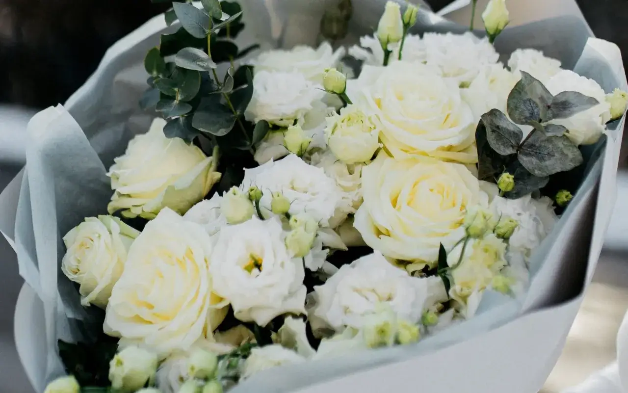 Elegancki eustoma bukiet w odcieniach bieli i kremu, ozdobiony zielonymi liśćmi eukaliptusa.